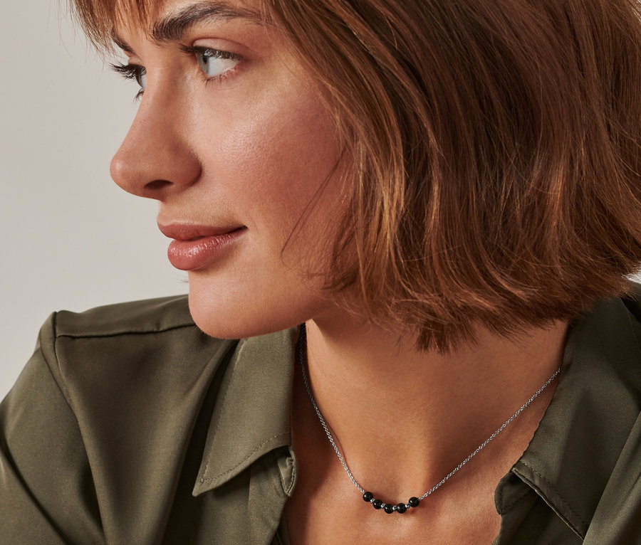 Profil d'une femme aux cheveux bruns et à la chemise verte portant une chaîne énergétique en obsidienne.