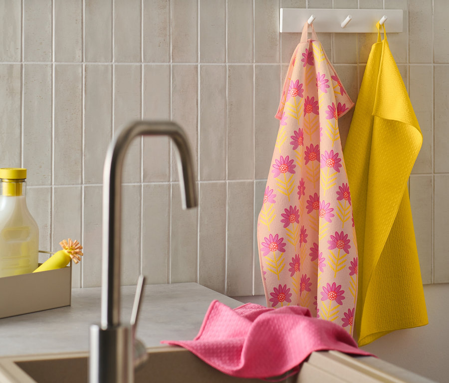 Un 3
Linges de cuisine à motifs floraux et un linge de cuisine jaune sont suspendus à un crochet. Un linge de cuisine rose repose sur le bord de l'évier.