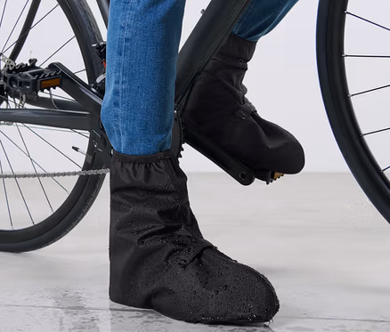 Pieds d'un cycliste en jean bleu et couvre-chaussures de pluie noirs sur un vélo.