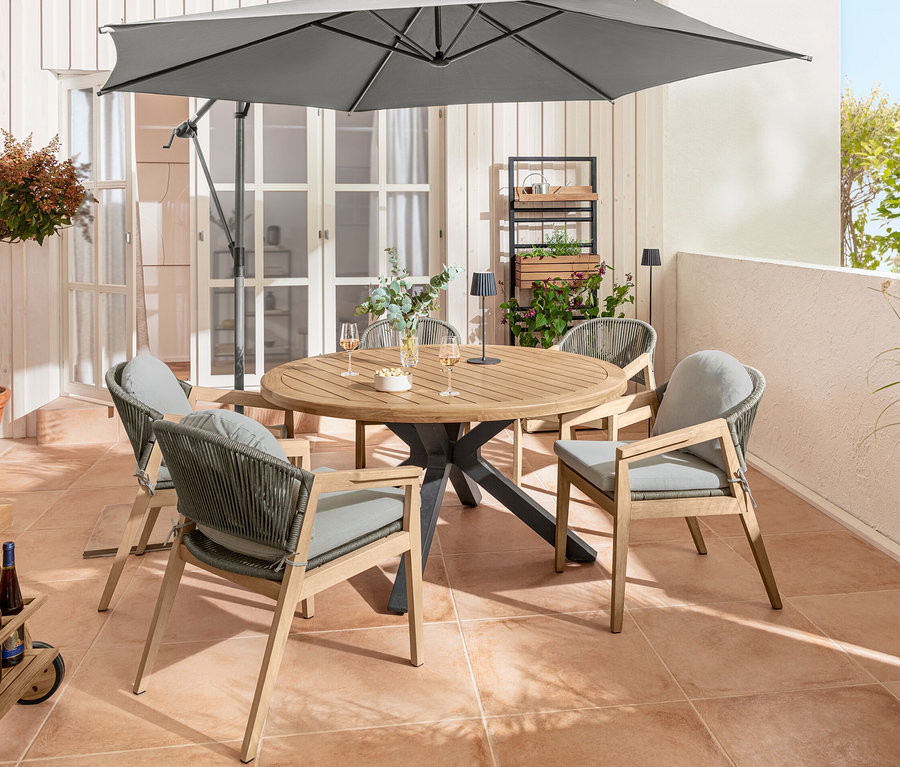 Terrasse avec table de salle à manger en teck avec pieds modernes en X, fauteuils de salon avec dossier arrondi et tressage textile et mur végétal « Elin » avec éléments à accrocher de façon flexible.