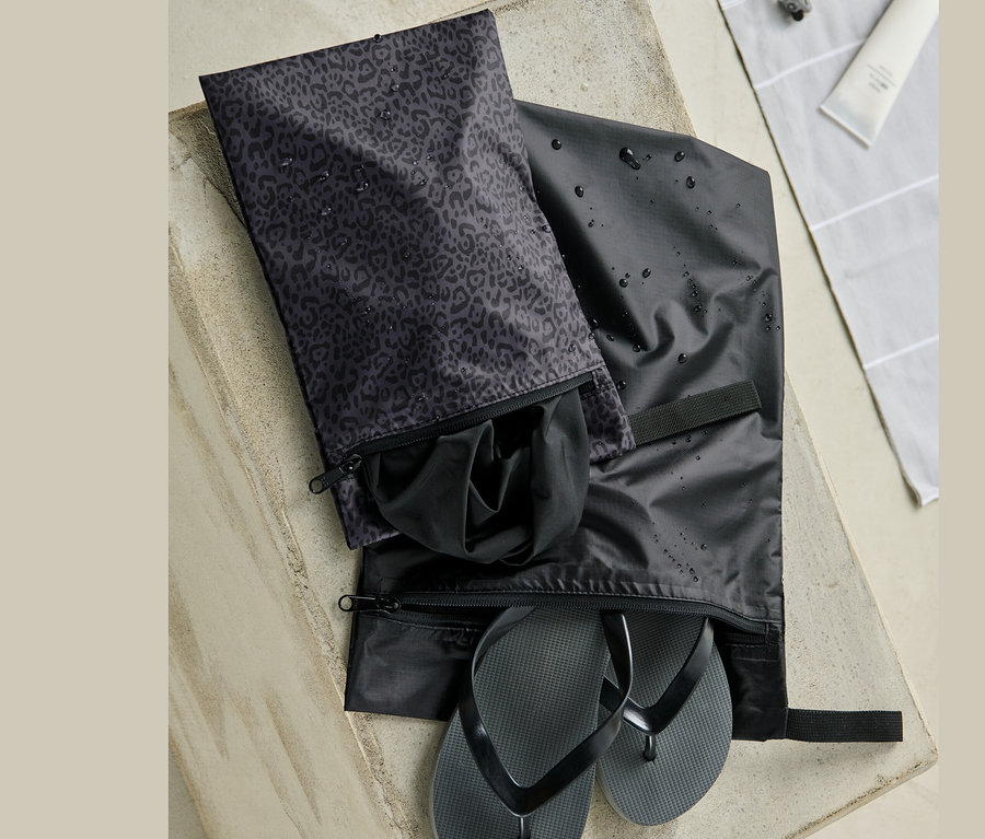 Deux sacs fourre-tout imperméables sur une surface en béton. L'un contient des tongs noires, l'autre des vêtements noirs.