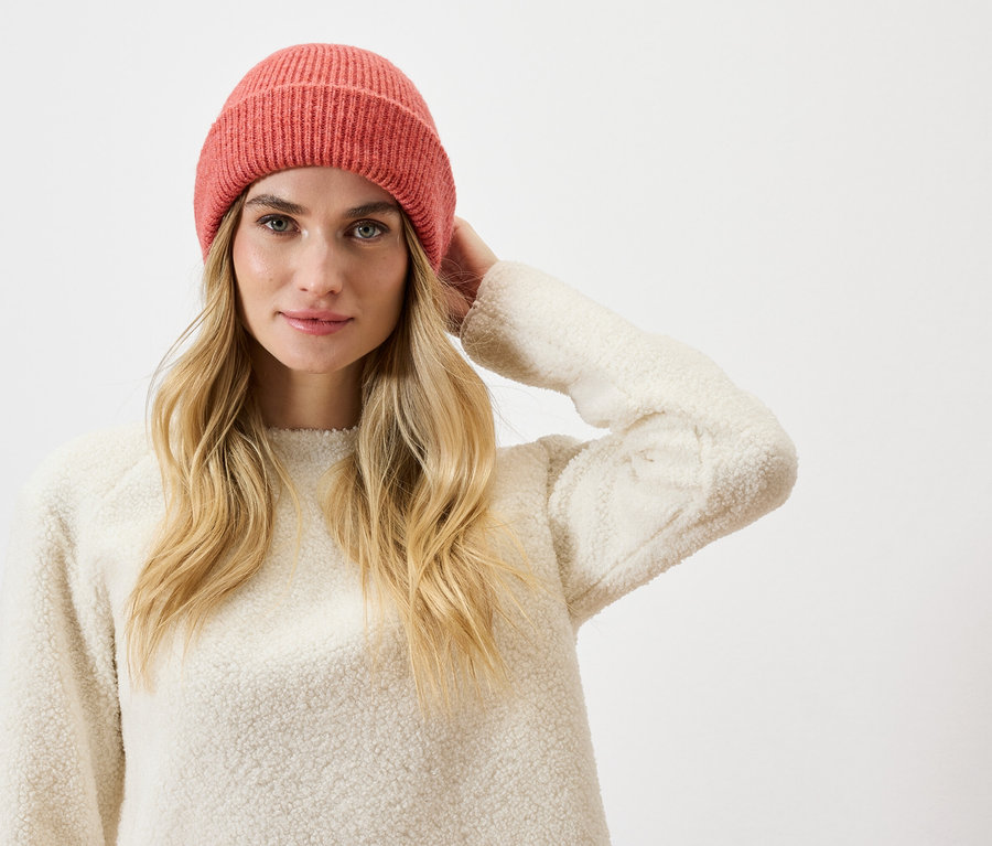 Femme blonde portant un bonnet tricoté rose et un pull crème.