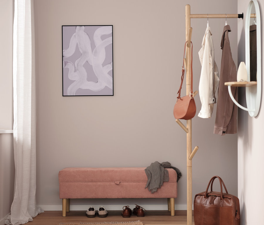 Un couloir avec un banc rose, des chaussures, un tapis marron, un porte-manteau, un sac à main et un miroir.
