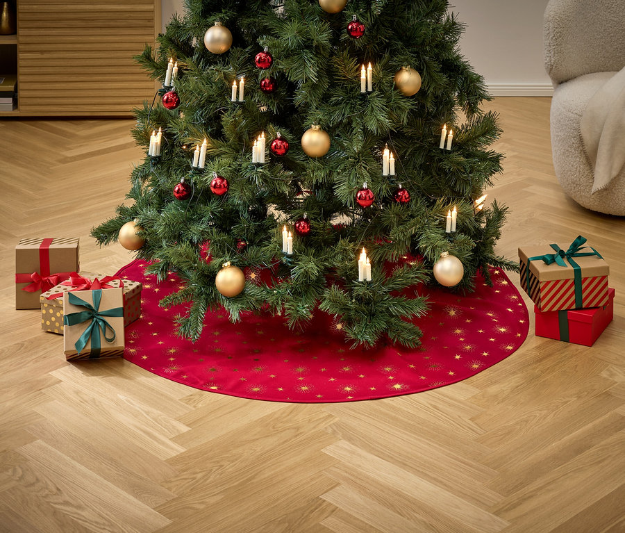 Un arbre de Noël décoré d'ornements rouges et dorés et de lumières se dresse sur une jupe rouge avec des étoiles dorées, entouré de cadeaux.
