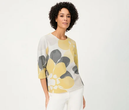 Une femme porte un sweat-shirt Olsen « Ottoman » à fleurs jaunes et grises sur fond blanc.