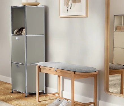 Une armoire grise avec des décorations est placée à côté d'un banc en bois avec un rembourrage gris et des chaussures blanches.