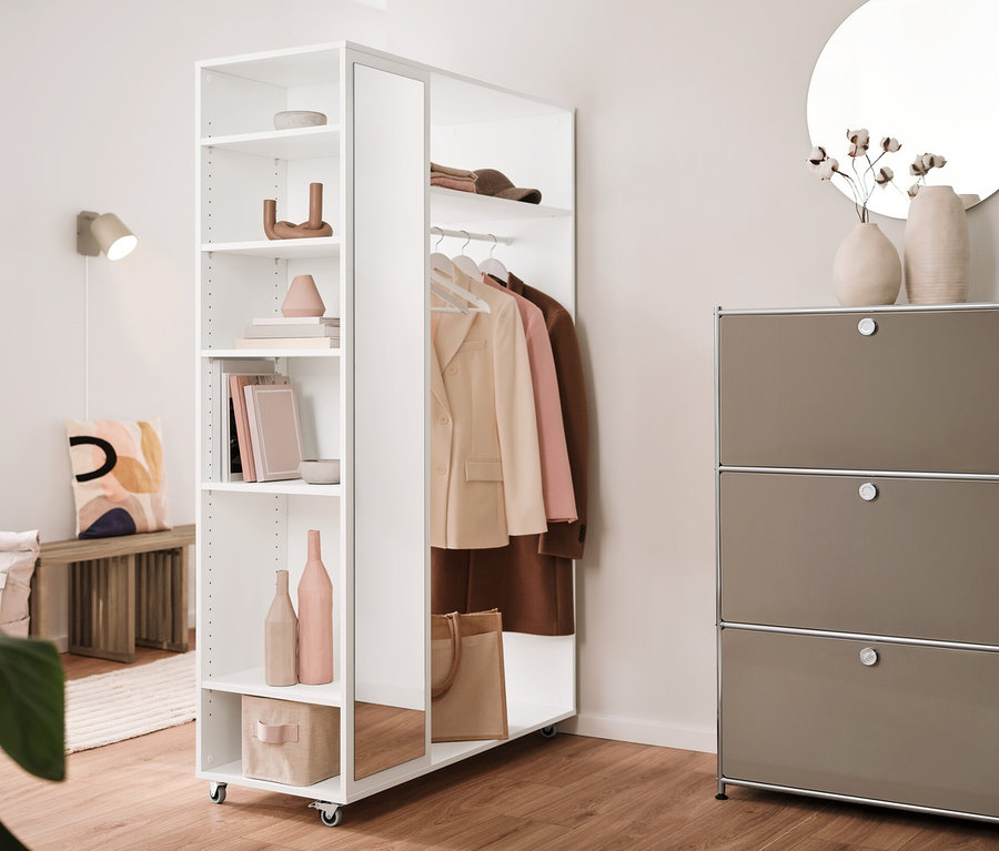 Intérieur avec une lampe murale en métal crème, une étagère en métal « CN3 » à 3 abattants et une garde-robe mobile avec miroir.