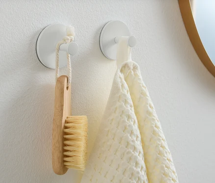 Deux crochets sont fixés sur un mur blanc. Une brosse en bois est suspendue à l’un d’eux et une serviette blanche à l’autre.