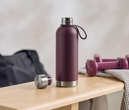 Une bouteille d'eau aubergine est posée ouverte à côté d'haltères et d'un sac de sport sur un banc en bois.