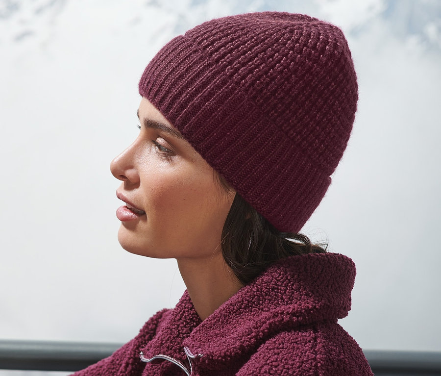 Une femme est assise à l'extérieur et porte un bonnet en maille rouge bordeaux.