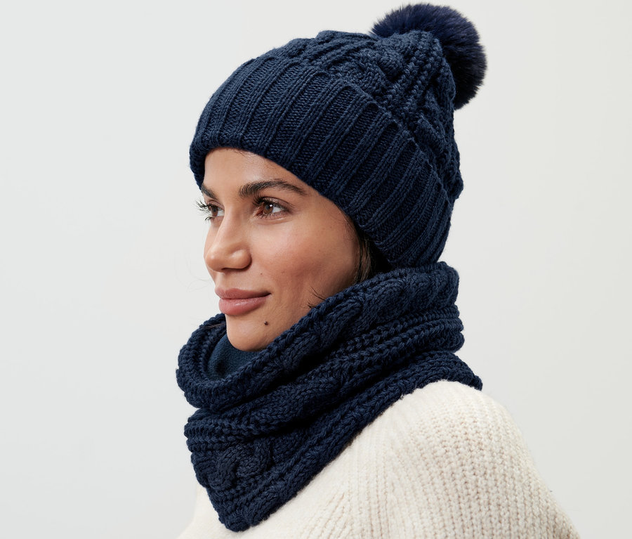 Une femme portant une écharpe tube en maille et un bonnet en maille assorti avec un pompon.