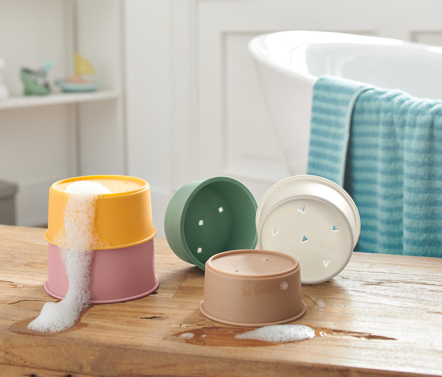 Sur une table en bois, des verres empilables pour jouer dans le bain, dont deux sont empilés avec de la mousse qui s'échappe du verre supérieur.
