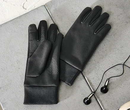 Deux gants thermiques de protection contre le vent pour enfant sont posés sur une surface grise à côté d'écouteurs et d'une partie d'un ballon de football.