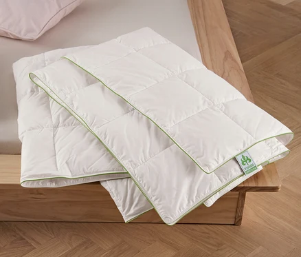Deux oreillers et un édredon d’été irisette® greenline de taille normale plié sur un lit.