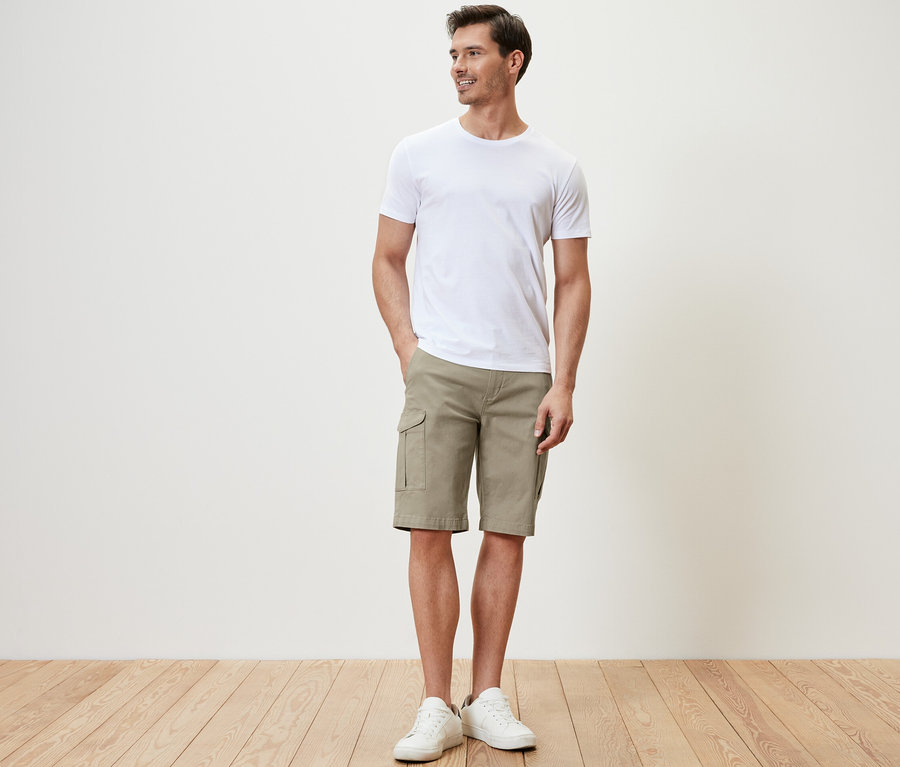 Un homme debout portant un short cargo beige et un t-shirt blanc.