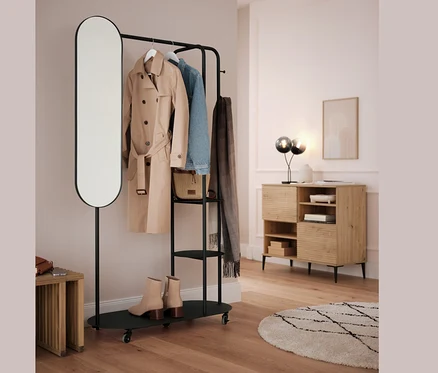 Portant noir avec miroir ovale et tabouret gigogne. Un manteau beige, une veste bleue et une écharpe grise sont suspendus à la barre.
