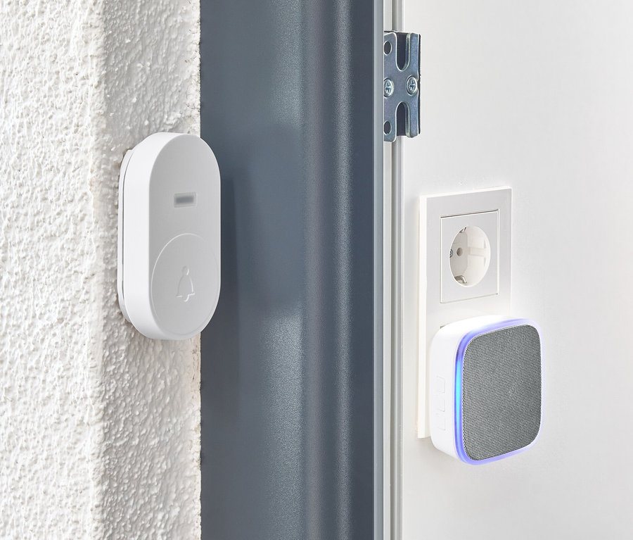 Un kit de sonnette sans fil blanche est fixé au mur à côté d'une porte.
