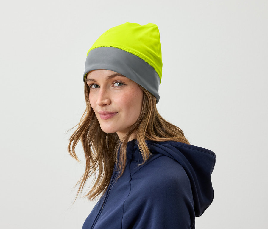 Portrait d'une femme aux cheveux bruns portant un bonnet gris et jaune et vêtue d'un sweat à capuche bleu.
