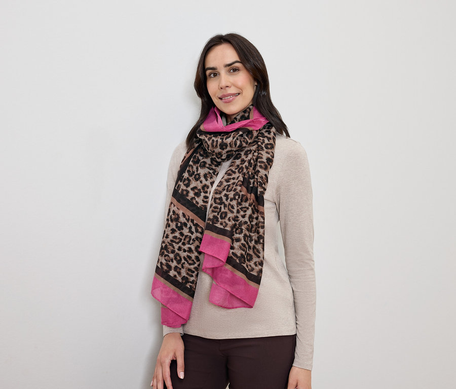 Une femme aux cheveux foncés pose avec un foulard à motif léopard avec des accents roses.