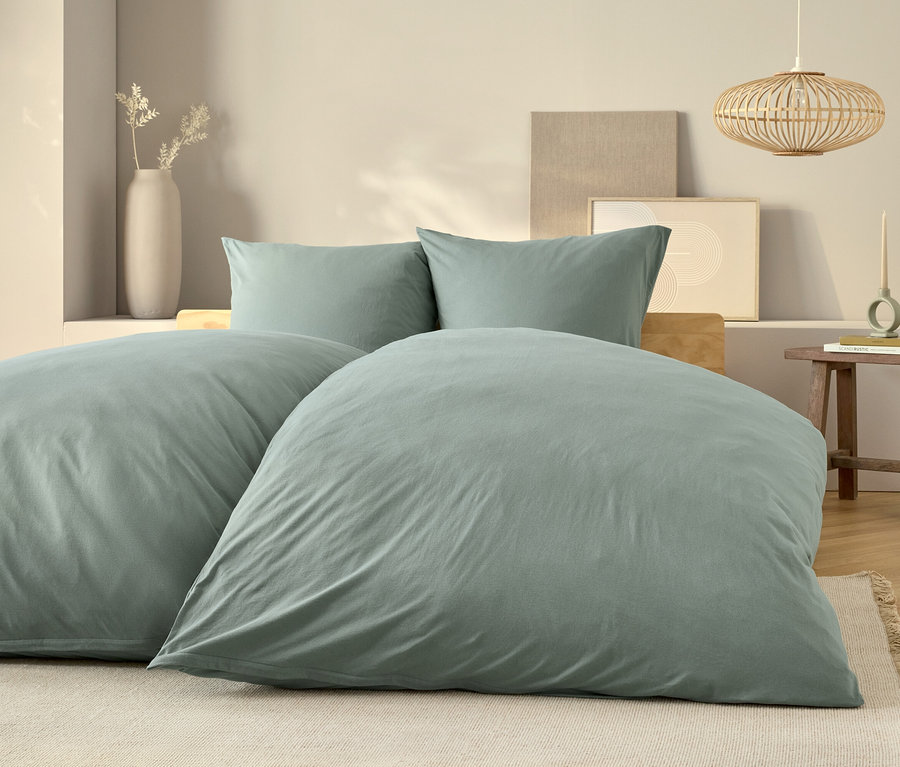 Linge de lit bleu clair sur un lit avec deux oreillers et une table de chevet en bois.