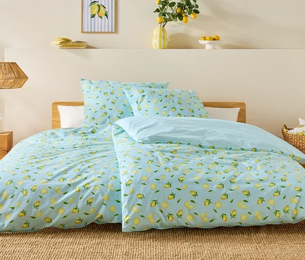 Lit avec une housse de couette bleu clair à motif citron, deux oreillers et une couverture bleu clair. Des bougies sont posées sur la table de chevet.