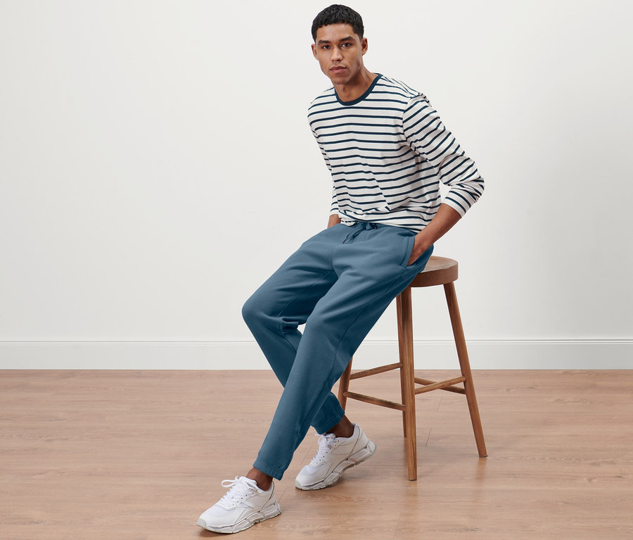 Un homme est assis sur un tabouret et porte un pantalon de survêtement.