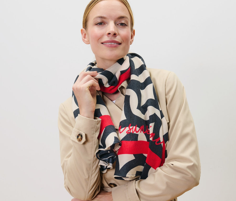 Femme posant en trench-coat beige avec une écharpe tissée imprimée.