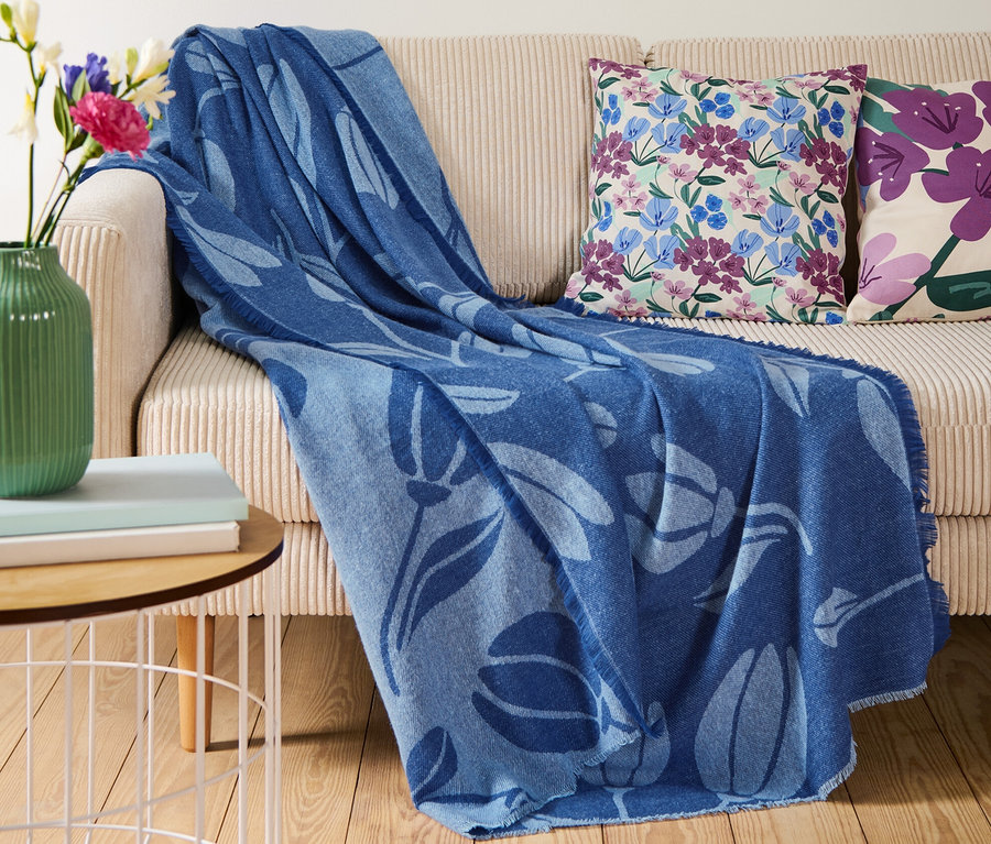 Sur un canapé beige se trouve une couverture d’intérieur bleue à fleurs avec des franges.