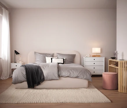 Chambre avec lit beige, linge de lit gris et tapis beige. En arrière-plan, table de chevet et commode blanches.