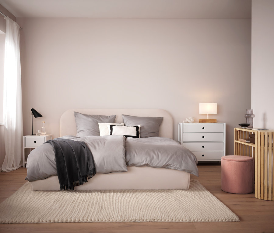 Chambre avec lit beige, linge de lit gris et tapis beige. En arrière-plan, table de chevet et commode blanches.