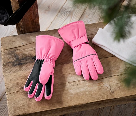 Sur un banc en bois reposent une paire de gants de ski roses et un bonnet tricoté blanc. Un bonnet noir est visible à l'arrière-plan.
