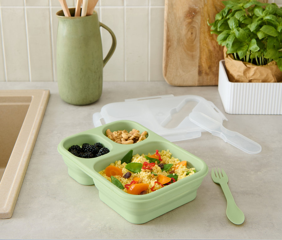 Une boîte repas pliable verte avec de la nourriture sur un comptoir de cuisine.