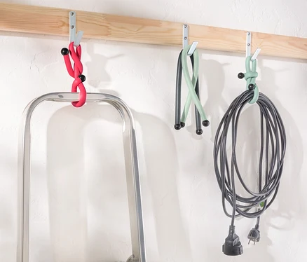 Une échelle est placée sous une latte en bois avec des crochets sur lesquels pendent des Power Kabelbinder en rouge, vert et noir.