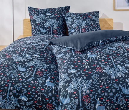 Lit avec des draps bleus à motifs de forêt, d'arbres, de cerfs et de lapins.