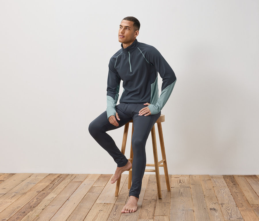 Un homme est assis sur un tabouret en bois et porte des sous-vêtements thermiques gris foncé.