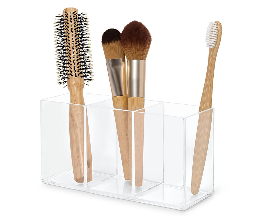 Brosse à cheveux, deux pinceaux de maquillage et une brosse à dents dans un organisateur en acrylique transparent.