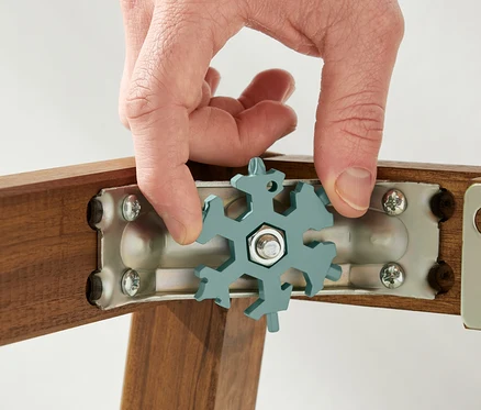 Une main tient une clé multifonctionnelle sur une vis sur un cadre en bois.
