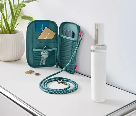 Un portefeuille vert ouvert posé sur une table blanche, rempli de cartes, de clés et d'un téléphone portable.