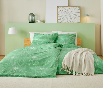 Un lit avec une housse de couette verte à motifs de fleurs blanches, une couverture blanche et une tête de lit vert clair.
