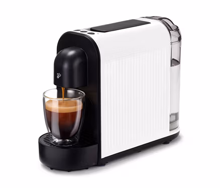 La machine à café Cafissimo now white remplit une tasse de café. La machine est blanche avec des accents noirs et un réservoir d'eau transparent.