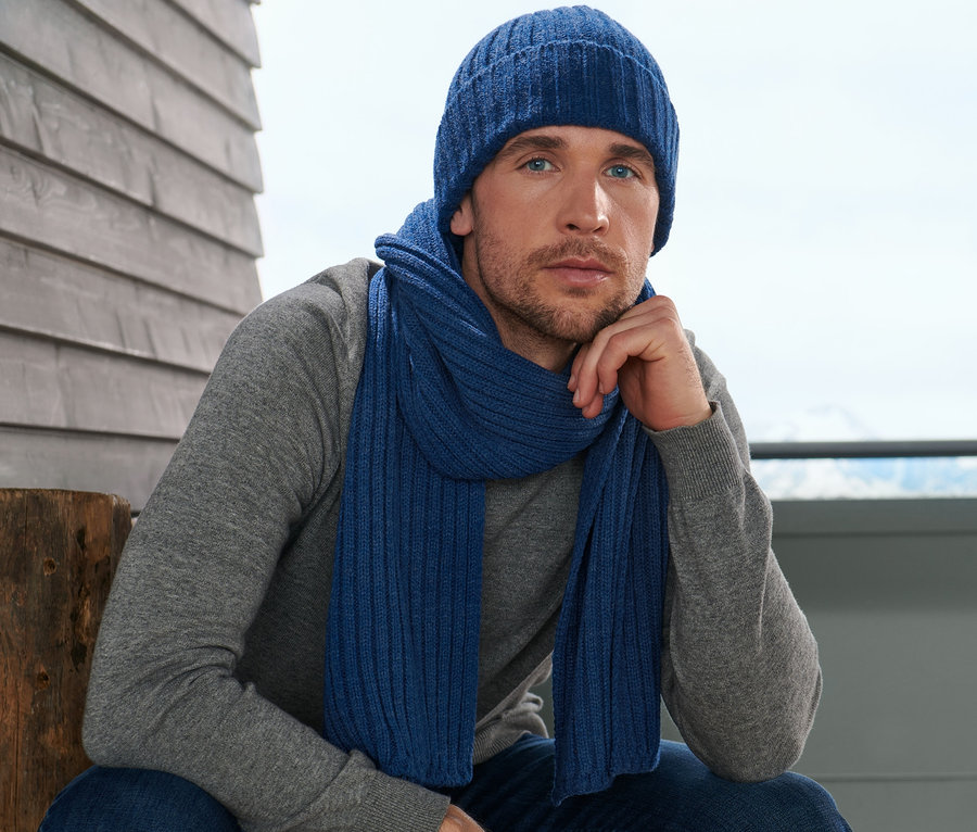 Un homme est assis et porte une écharpe en maille et un bonnet.