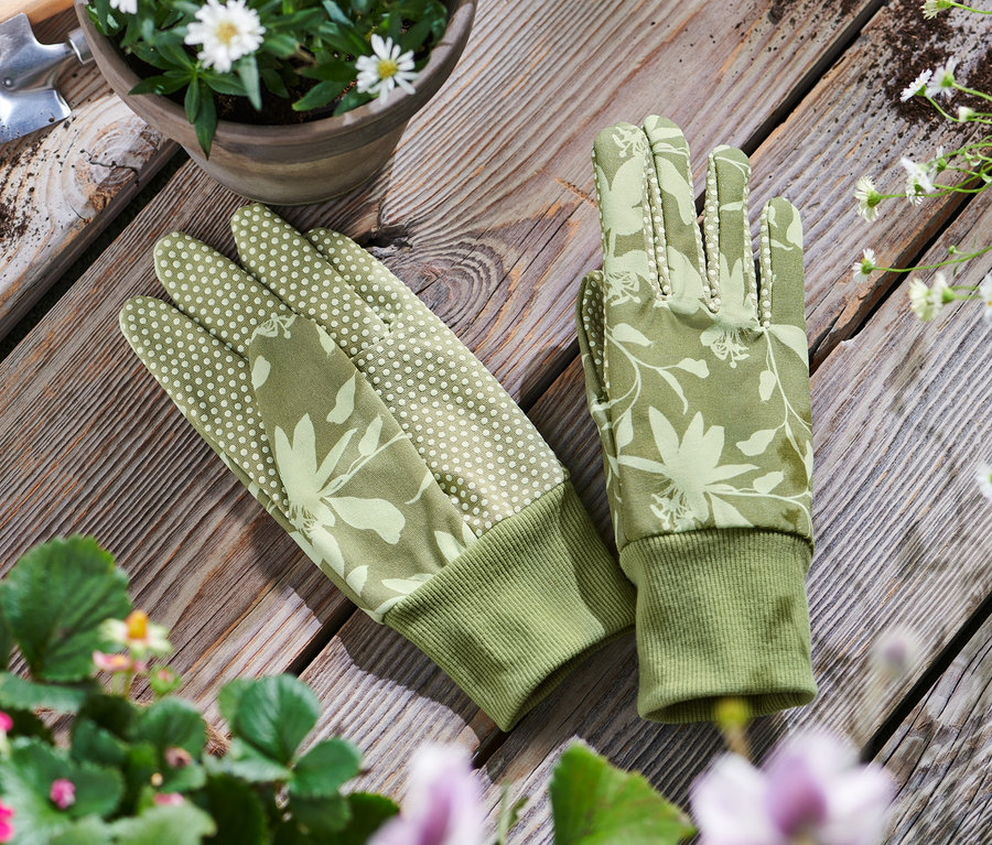 Des gants de jardinage reposent sur une table en bois à cÎté d'un pot de fleurs et d'outils de jardinage.