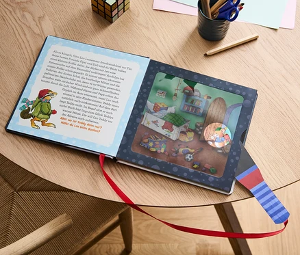 Le livre «
on Leo Lausemaus – mein Taschenlampenbuch
on » est ouvert sur une table à côté de crayons de couleur et d'un cube.