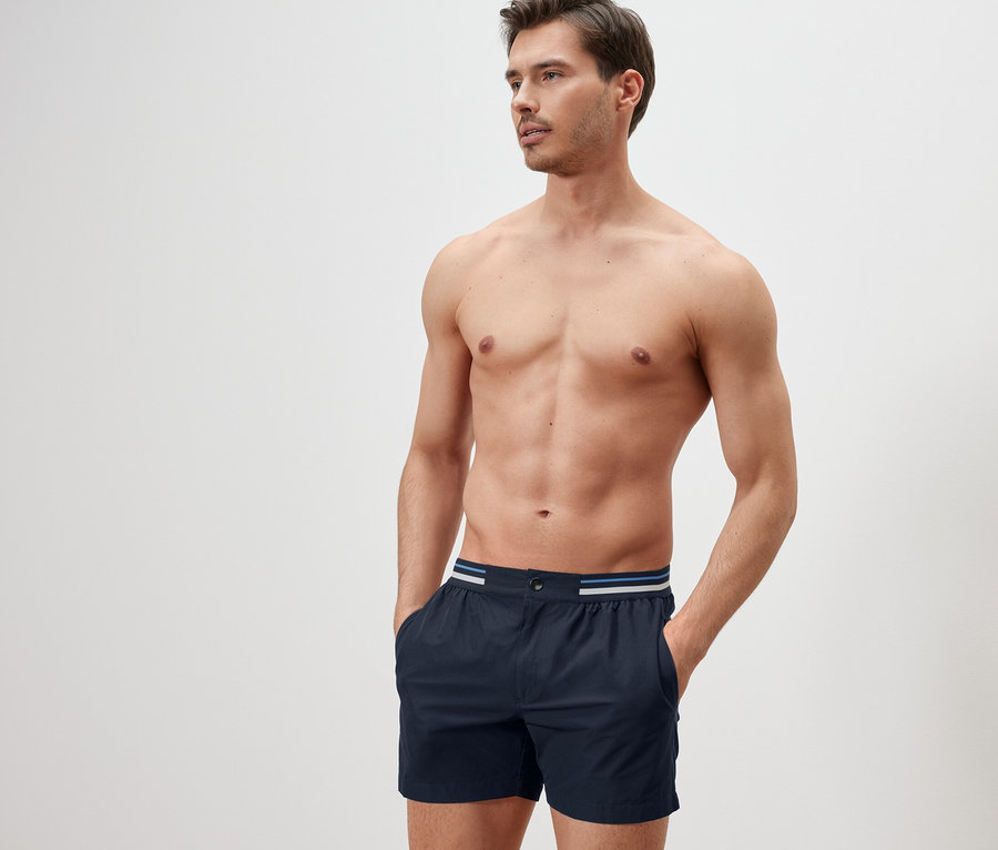 Homme avec les mains dans les poches d'un short de bain bleu foncé.