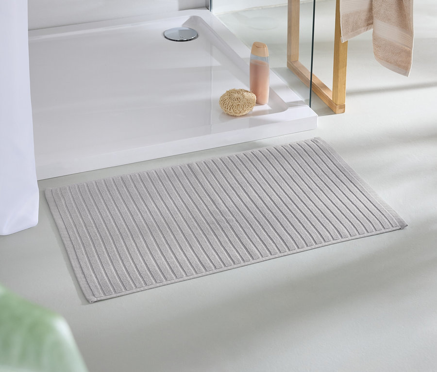Un tapis de bain beige est posé sur le sol à côté d'une douche.