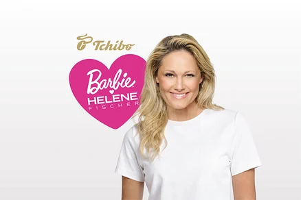 Une femme blonde souriante vêtue d'un t-shirt blanc se tient à côté d'un logo en forme de cœur rose portant l'inscription « Barbie HELENE FISCHER ». Au-dessus du cœur se trouve le logo « Tchibo ».