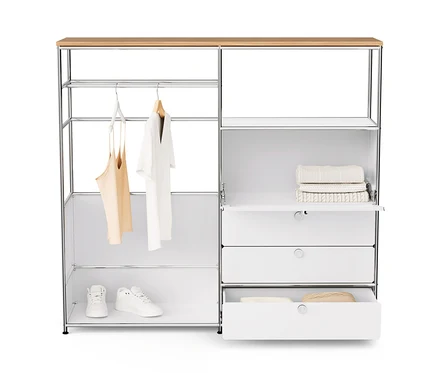 Commode en métal blanche « CN3 » avec plateau en bois, tringle à vêtements, abattant et 3 tiroirs. Des vêtements sont suspendus à la tringle, des chaussures et des pulls sont posés sur les étagères.