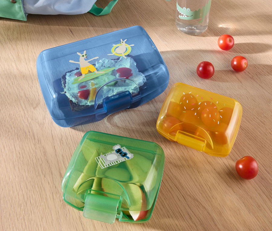 Trois boîtes à lunch sont posées sur une table, à côté d'une bouteille d'eau et d'un sac à dos.