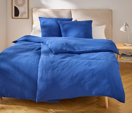Literie bleue avec deux oreillers sur un lit avec une tête de lit beige. Une lampe est posée sur la table de chevet.
