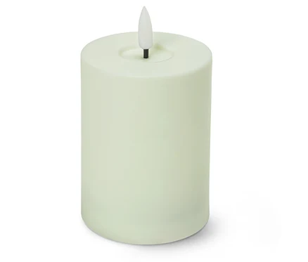 Une bougie pilier vert clair avec une flamme LED blanche en forme de goutte est posée devant un fond blanc.
